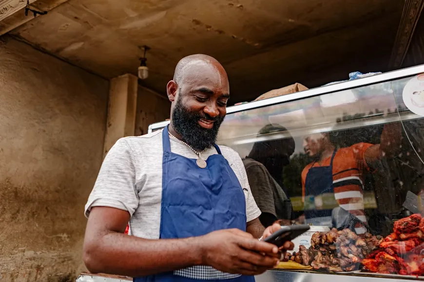 A street vendor engages with his mobile phone, potentially managing digital transactions for his small business. This scene reflects the growing intersection of technology and informal economies.